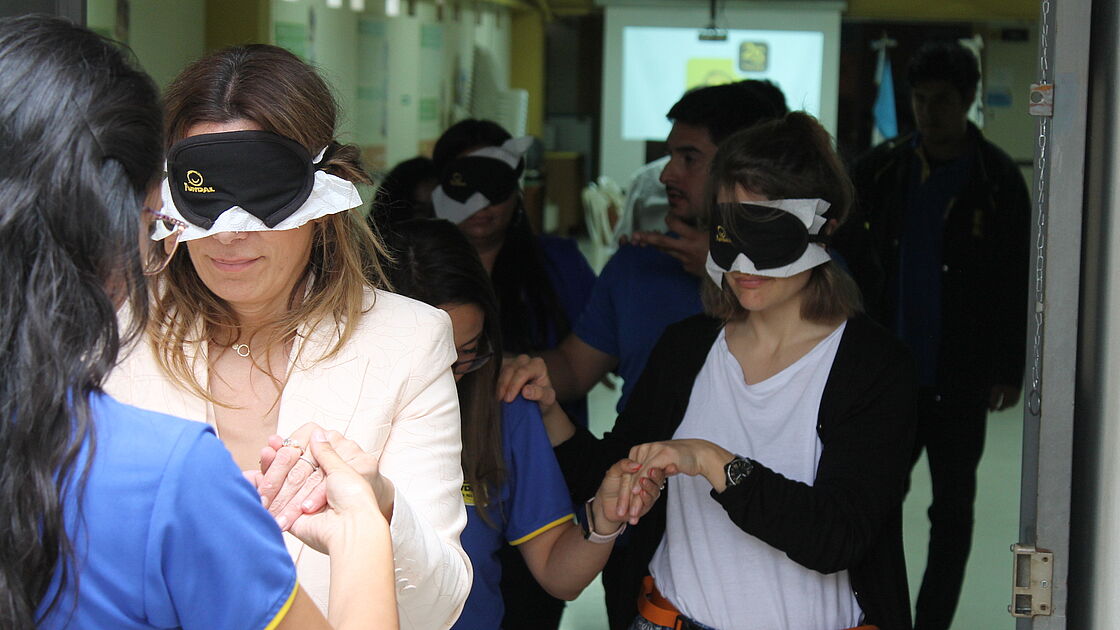 Two women with blind folds are being led by a person in a simulation exercise.   