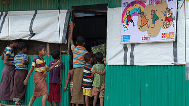 children at the door look inside as children play in the makeshift building