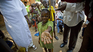 A young 7 year old boy holds out his hand, where there is a pill in his palm.