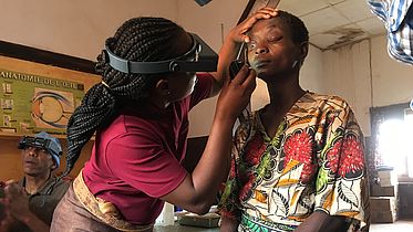 This photo shows a lady wearing googles inspecting the eyes of a patient.