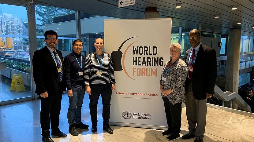 Group of people stand in front of a World Hearing Forum banner