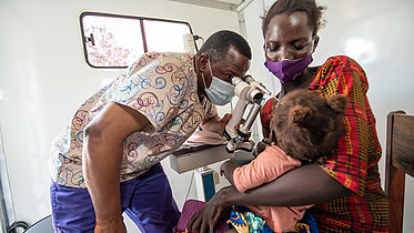 An eye nurse is examining a little baby's eyes in a mobile van which is a clinic.