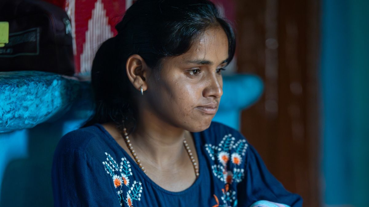 Ein Mädchen in blauer, bestickter Tunika, gestreifter Pluderhose und Pferdeschwanz sitzt an eine gemauerte Bank angelehnt.