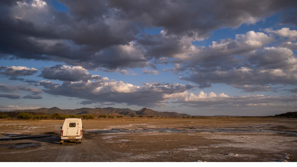 Ein Auto in savannenartigem Gelände, darüber ein weiter Wolkenhimmel.