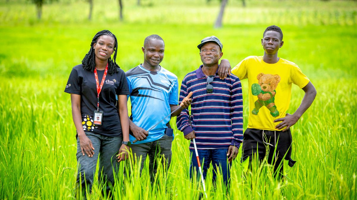 Four people standing in last green rice field. 