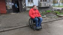 A man in a wheelchair on the side of the road in front of a house.