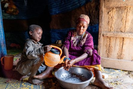 Ein kleiner Junge lässt Wasser aus einer Kanne über die Hände einer Frau laufen, damit sie sich waschen kann.