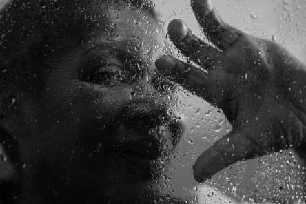 Gesicht einer Frau aus Lateinamerika hinter einer Glasscheibe, an die sie mit der Hand fasst