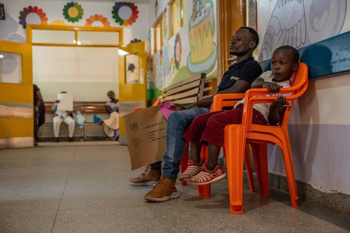 Ein Mann und ein Junge sitzen auf Plastikstühlen auf einem Flur.