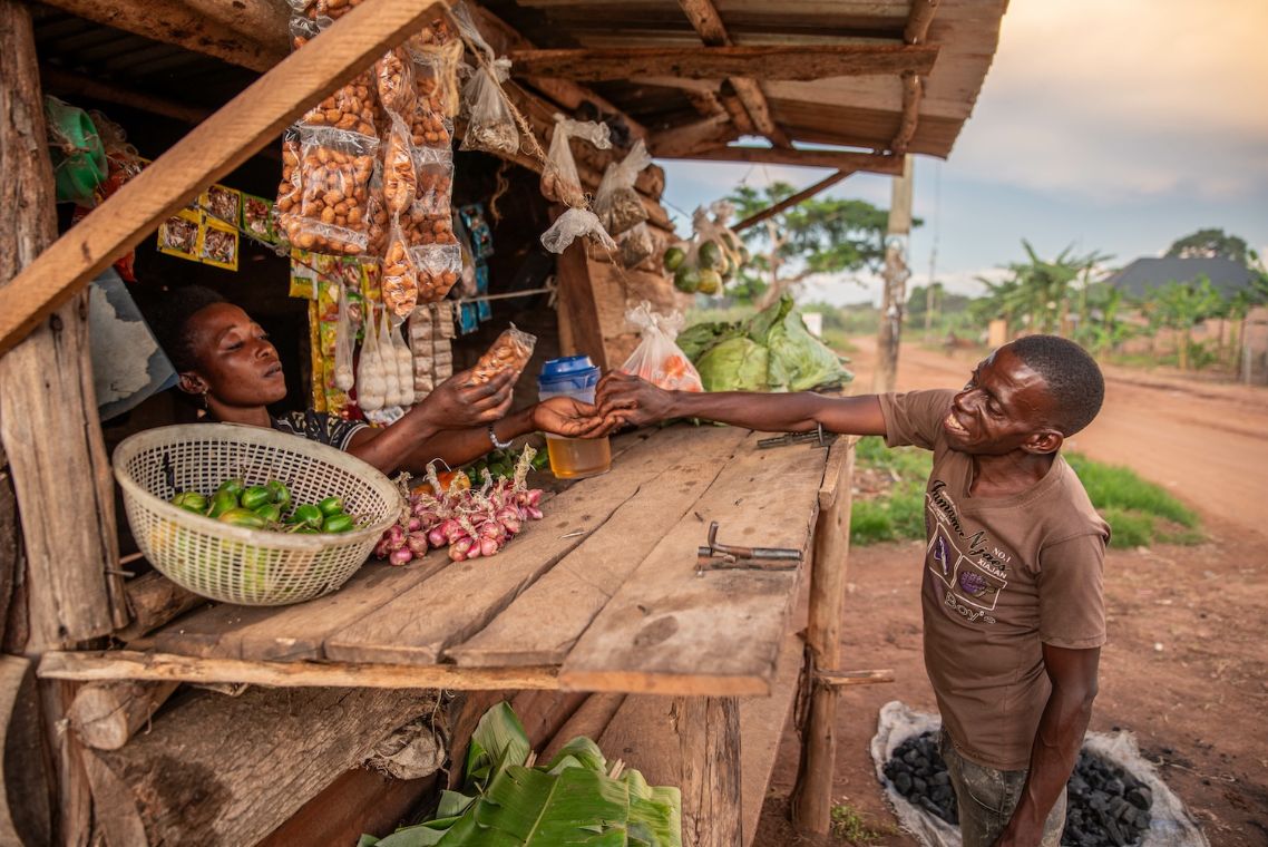 Eine Frau reicht einem Mann ein Päckchen Nüsse über die geöffnete Klappe ihres Kiosks.