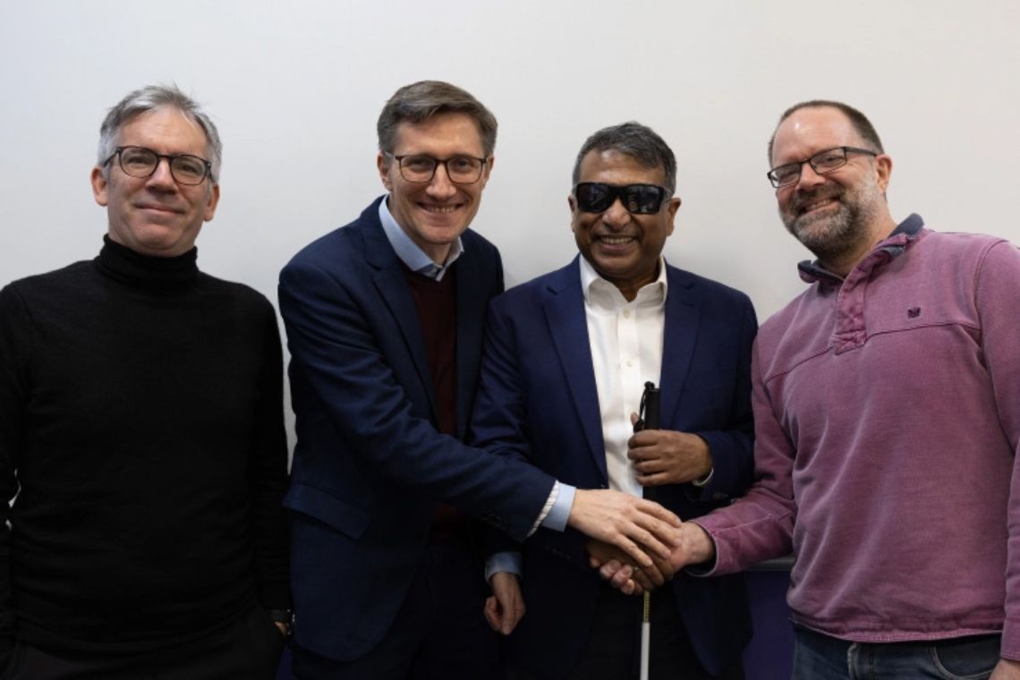 Vier Männer stehen nebeneinander, zwei davon reichen sich die Hände. Einer der Männer trägt eine Sonnenbrille.