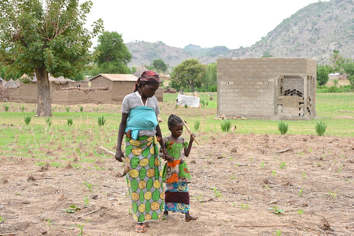 Ein etwa achtjähriges Mädchen geht an der Hand einer Frau über ein Feld.