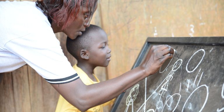 A woman and a child write on a blackboard with chalk