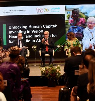 A group of people at a conference. Words on the banner behind the speakers read: Unlocking Human Capital. Investing in vision, hearing and inclusion for every child in Africa