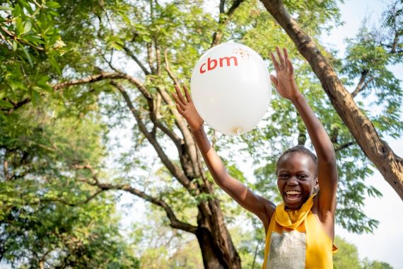 Ein etwa neunjähriges Mädchen lacht beim Fangen eines Luftballons, auf dem "CBM" steht.