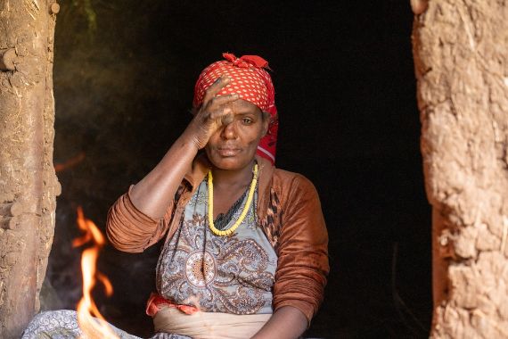 Eine Frau mit gepunktetem Kopftuch reibt sich mit der Hand am Auge.