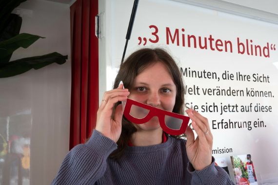 Eine junge Frau hält eine undurchsichtige Pappbrille vors Gesicht.