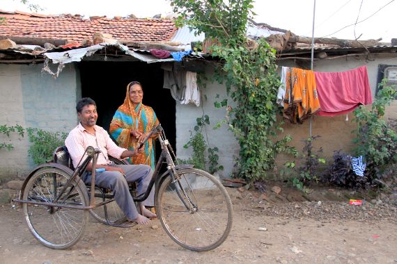 Ein indischer Mann sitzt in einem Tricycle. Neben ihm steht eien indische Frau.