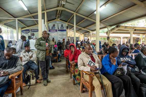 Volle Wartehalle: Die Menschen eng nebeneinander auf Holzbänken.