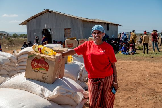 A woman wearing a red T-shirt stands next to a stack of food