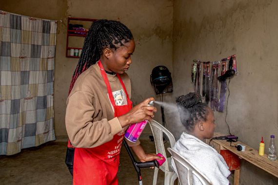 A hair dressing spraying a clients hair inside a salon. The hairdresser is standing with the support of a walking cane