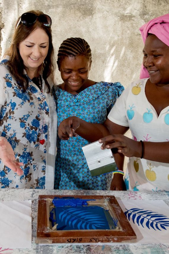 Drei Frauen stehen nebeneinander und schauen auf einen bedrucktes Tuch.