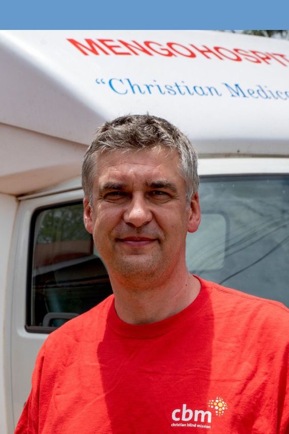 Ein Mann steht vor einem LKW mit der Aufschrift "Mengo Hospital - Mobile Clinic"