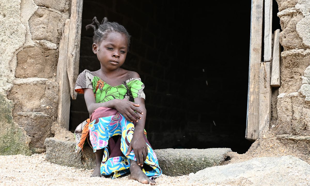 Ein etwa achtjähriges Mädchen sitzt im Türrahmen einer gemauerten Hütte.