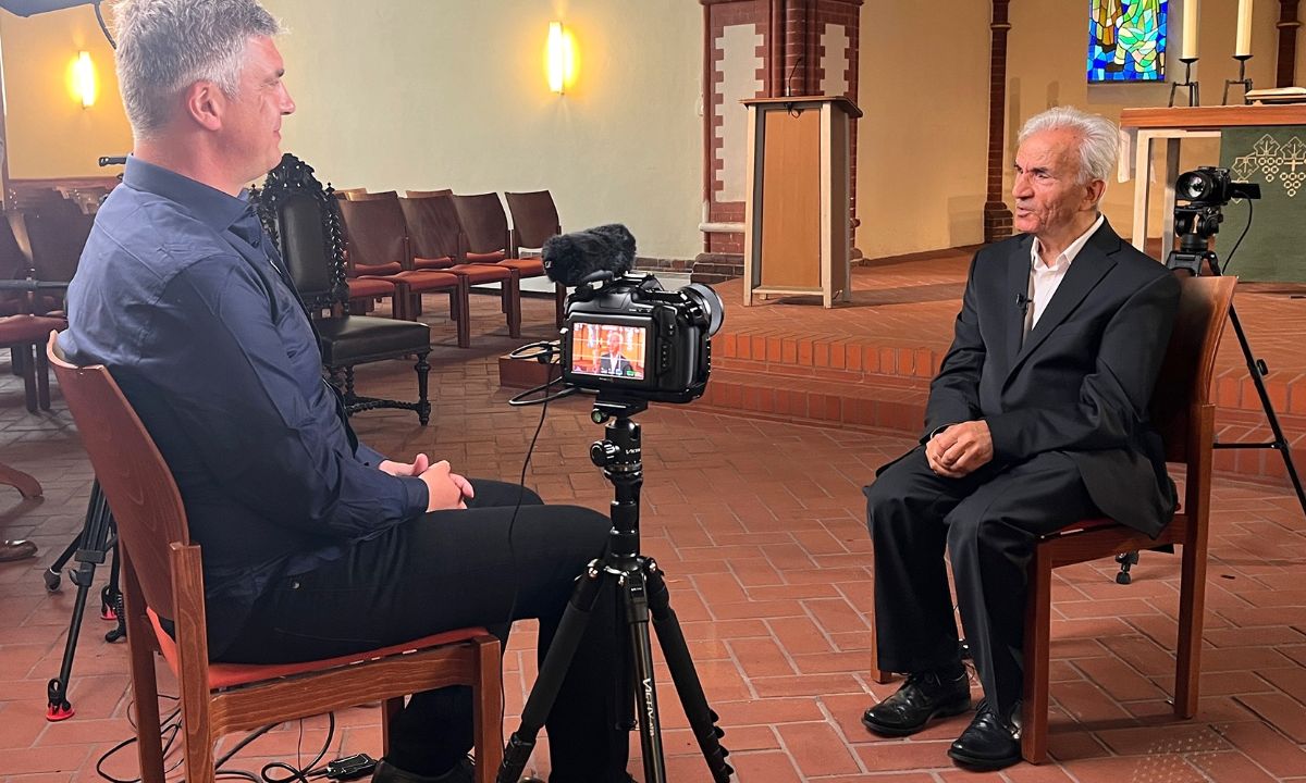 Zwei Männer sitzen sich in einem Kirchenraum gegenüber, zwischen ihnen steht ein Mikrofon.