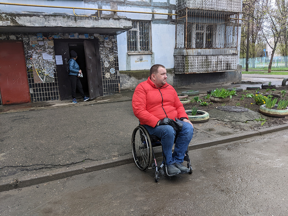 A man in a wheelchair on the side of the road in front of a house.