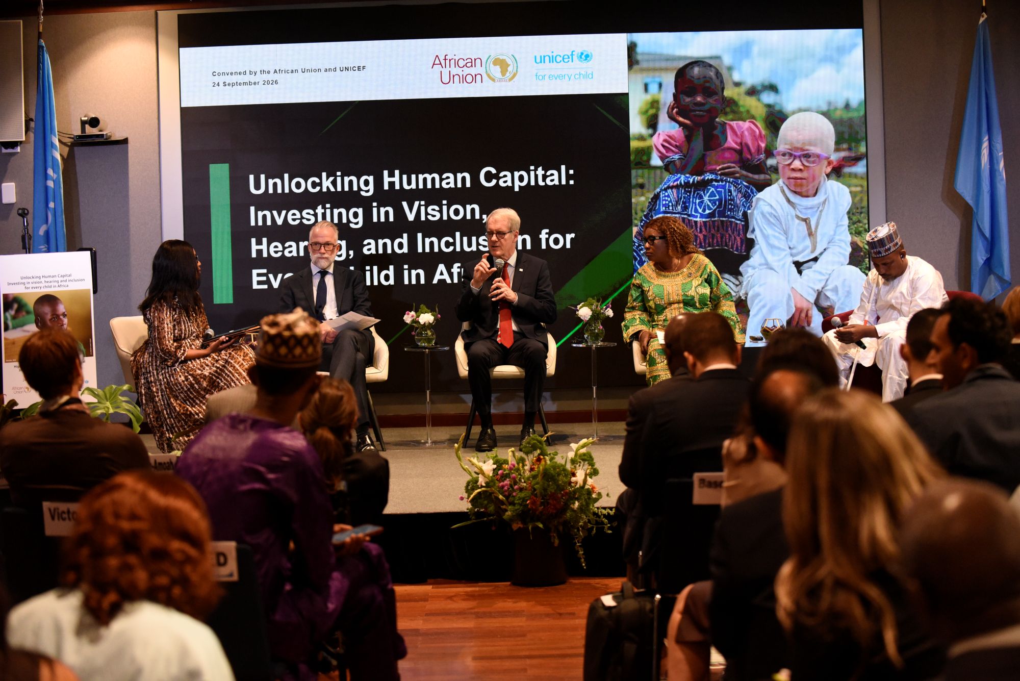 A group of people at a conference. Words on the banner behind the speakers read: Unlocking Human Capital. Investing in vision, hearing and inclusion for every child in Africa