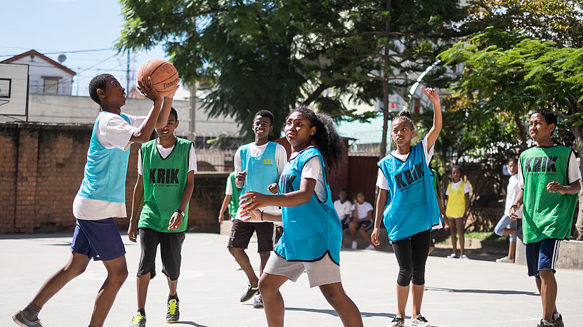 This photo shows young Madagascar girls and boys playing basketball on a court.