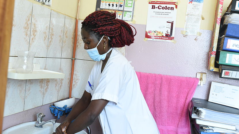This photo shows a nurse wearing a mask and washing her hands at a basin in an hospital