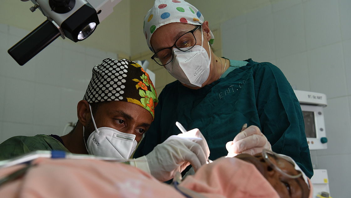 Two doctors are examining the ear of a patient lying on a hospital bed
