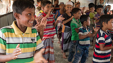 This photo shows a group of kids standing in lines and clapping their hands.