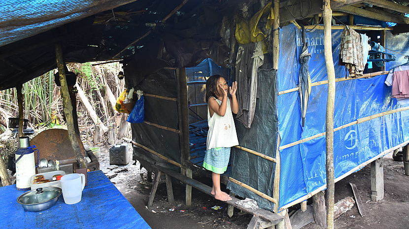 A girl affected by congenital cataract and a mental disability stands on a raised wood plank in her family's temporary shelter 