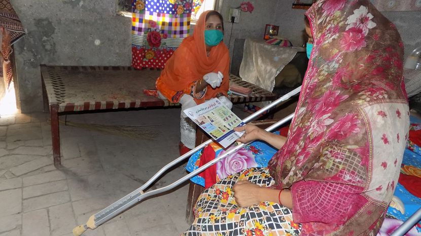 This photo shows 2 women - one with a physical disability, who is reading a COVID-19 information leaflet.
