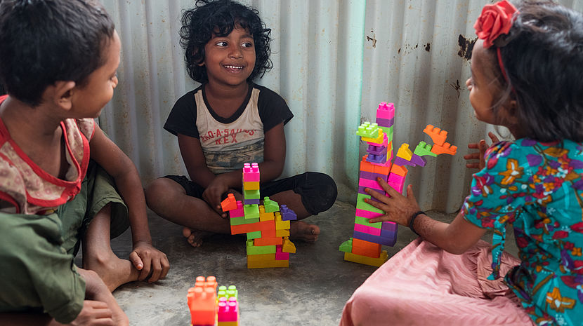 Photo of 3 young 8 year old girls sitting on the floor smiling, and playing with building blocks.