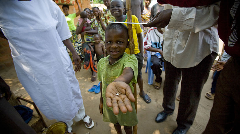 A young 7 year old boy holds out his hand, where there is a pill in his palm.