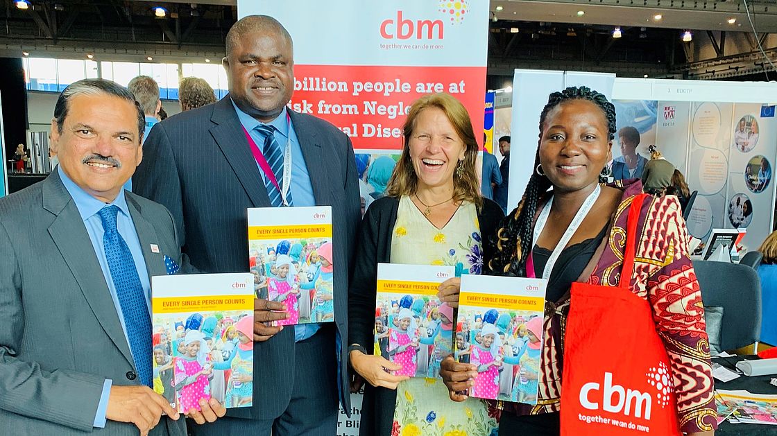 Three CBM staff and the director of CBM partner HANDS each hold up CBM's 2019 NTD report in front of a booth at the NNN conference.