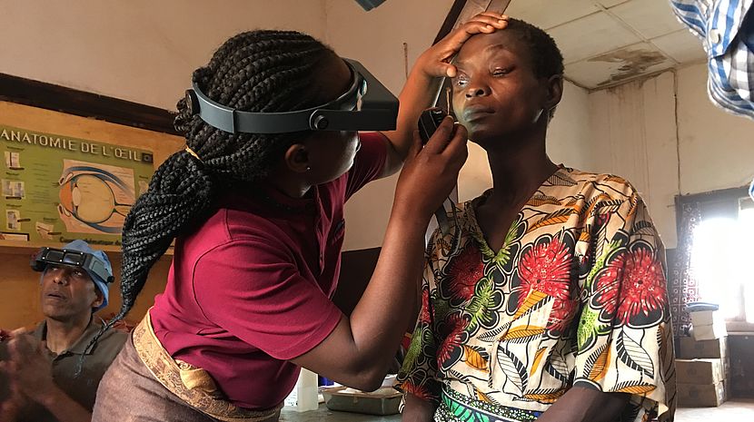 This photo shows a lady wearing googles inspecting the eyes of a patient.