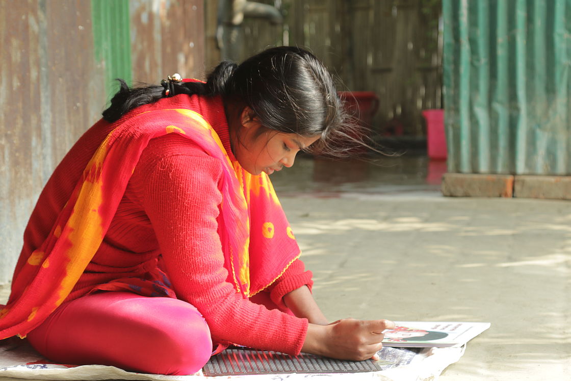 This photo shows a young girl sitting on the ground reading a text in Braille.