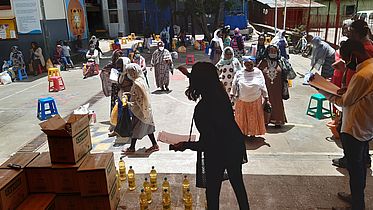 This photo shows people standing far apart from one another. There are bottles of food oil and other food packages ready for distribution.